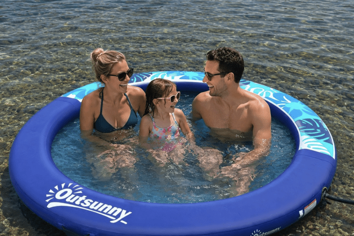 Three people smiling in a small inflatable pool by the sea.