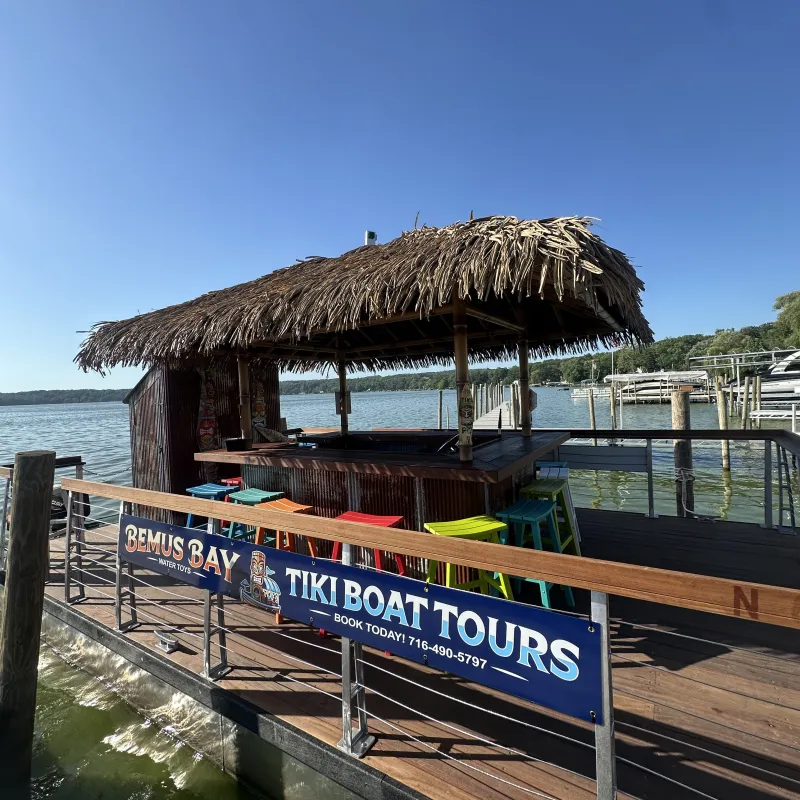 Thatched-roof tiki bar on a waterway with colorful stools and a tour sign.