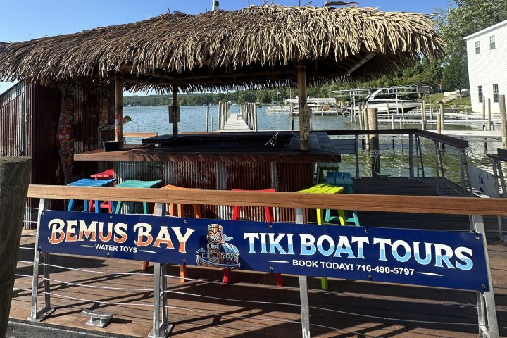 Tiki boat tour dock with straw roof and colorful chairs under a clear blue sky.