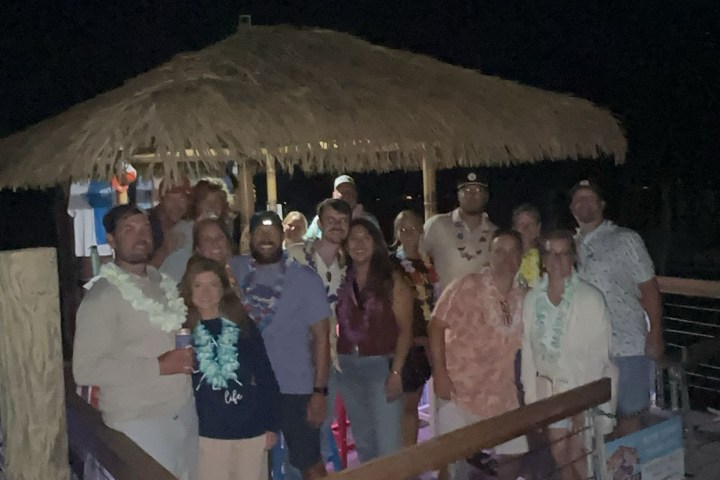 Group of people posing under a tiki hut at night.